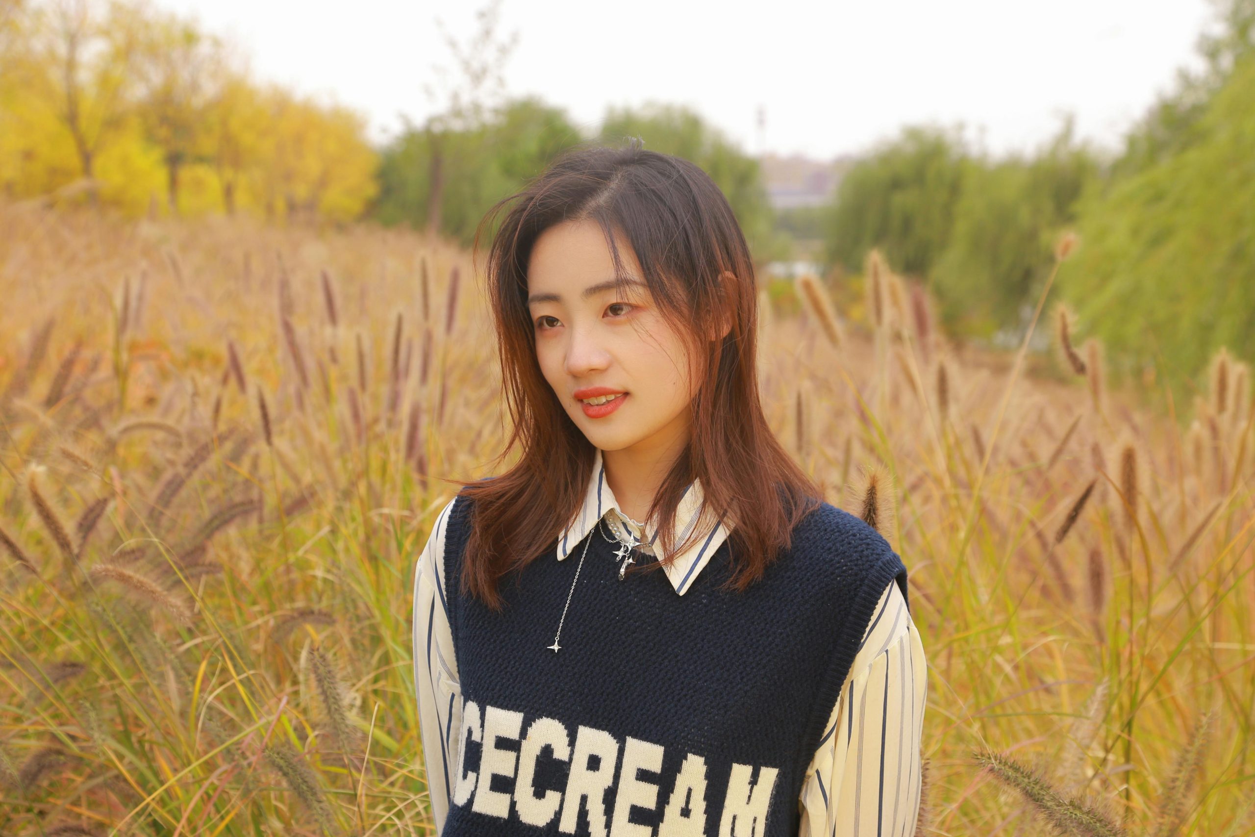 A young woman in a sweater smiles in a sunny autumn meadow in Zibo, China.